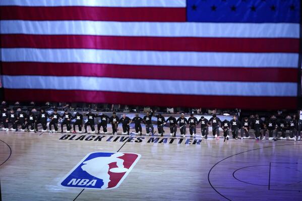 FILE - Members of the Orlando Magic and Brooklyn Nets kneel around a Black Lives Matter logo during the national anthem before the start of an NBA basketball game, in Lake Buena Vista, Fla., July 31, 2020. (AP Photo/Ashley Landis, Pool, File)