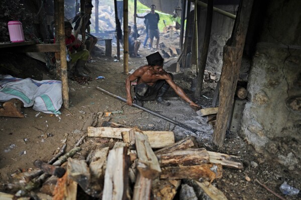 A worker puts firewood into a furnace at a patchouli oil refinery in Simboro, West Sulawesi, Indonesia, Thursday, Feb. 27, 2025. (AP Photo/Dita Alangkara)