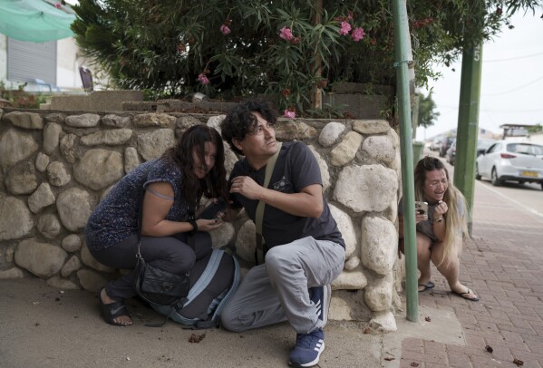 Israelis take cover from the incoming rocket fire from the Gaza Strip in Ashkelon, southern Israel, Wednesday, Oct. 11, 2023. (AP Photo/Leo Correa)