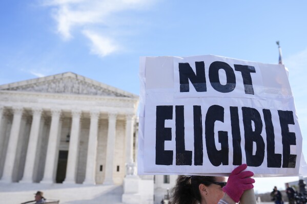 FILE - A demonstrator holds a sign outside of the U.S. Supreme Court, Feb. 8, 2024, in Washington. A pair of recent U.S. Supreme Court actions has opened the door to a new legal frontier in which local and state officials can be disqualified from office for life for engaging in "insurrection" or providing "aid and comfort" to enemies of the Constitution, based on a post-Civil War-era provision of the nation's foundational legal document and how the courts interpret it. (AP Photo/Mariam Zuhaib, File)