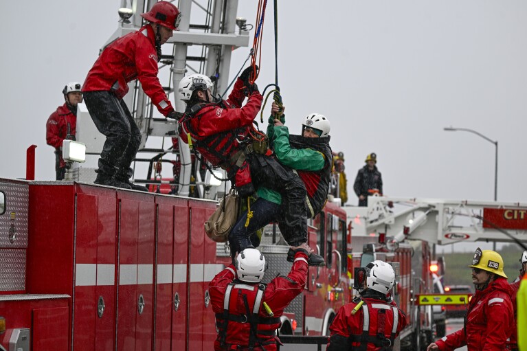 Riverside County Firefighters use a crane on a ladder truck to rescue people who became stranded on a small island in the middle of the Santa Ana River near Van Buren Street in Riverside, Calif., when the river waters rose due to rain on Monday, Feb. 5, 2024. (Anjali Sharif-Paul/The Orange County Register via AP)
