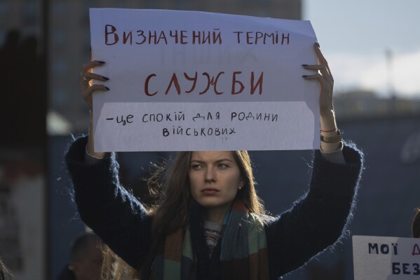 Kateryna Zahidko, who waits for her husband to return from the frontline, holds a poster reading "Defined period of service means calmness for families of soldiers" while attending a meeting in Independence square in Kyiv, Ukraine, Friday, Oct. 27, 2023. Families of Ukrainian servicemen gathered to demand their loved ones return home after serving 18 months in the military as the war with Russia nears its second year. (AP Photo/Alex Babenko)