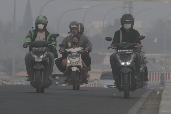 Riders wear mask as they pass through the haze from forest fires in Palembang, South Sumatra, Indonesia, Friday, Oct. 6, 2023. Indonesia denied Friday that forest and peat fires on Sumatra and Borneo islands were causing the haze in Malaysia, after the neighboring government sent a letter complaining about the air quality and asking to work together to deal with the fires. (AP Photo/Muhammad Hatta)