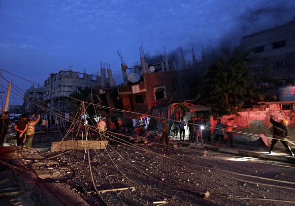 People gather as Palestinian civil defense crews try to extinguish fire in a house that was hit by an Israeli airstrike in Khan Younis, southern Gaza Strip, Sunday Oct. 8, 2023. (AP Photo/Yousef Masoud)