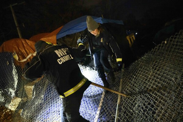 Minneapolis Crime Lab investigators climb over a downed fence while investigating a homicide Tuesday, Dec. 12, 2023 in the Nenookaasi encampment in Minneapolis. A man was shot to death at the large homeless encampment, days before it was scheduled to be removed. (Aaron Lavinsky/Star Tribune via AP)