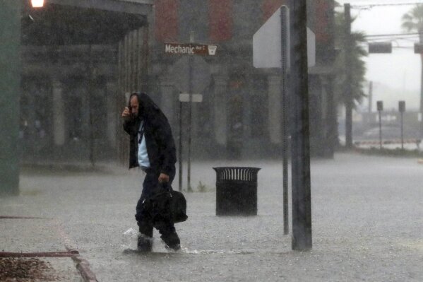 A man attempts to protect himself from the rain while walking across a flooded 20th Street in Galveston, Texas, Thursday, Sept. 19, 2019, as rains from Tropical Depression Imelda inundated the island. (Kelsey Walling/The Galveston County Daily News via AP)