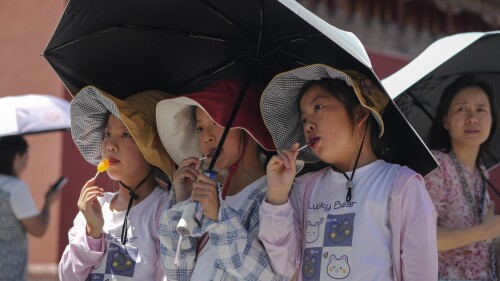 Children wearing sun hats and carrying an umbrella pose for a souvenir photo near the Forbidden City on a sweltering day in Beijing, Friday, July 7, 2023. Earth's average temperature set a new unofficial record high on Thursday, the third such milestone in a week that already rated as the hottest on record. (AP Photo/Andy Wong)