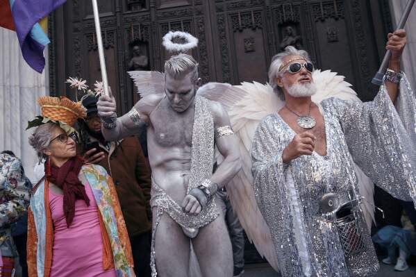 A woman looks at revelers wearing decorated hats and costumes as they participate in the annual Easter Parade and Bonnet Festival in front of St. Patrick's Cathedral on Sunday, April 20, 2025, in New York. (AP Photo/Andres Kudacki)