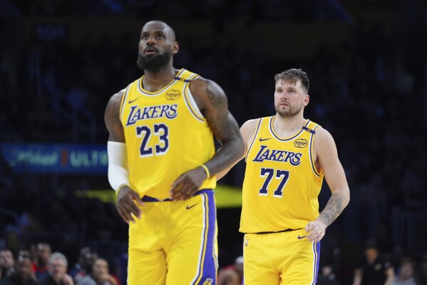 Los Angeles Lakers' LeBron James (23) and Luka Doncic (77) watch action during the second half of an NBA basketball game against the New Orleans Pelicans Tuesday, March 4, 2025, in Los Angeles. (AP Photo/Jae C. Hong)