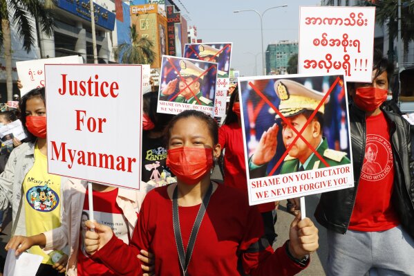 A protester holds a placard with an image of Myanmar military Commander-in-Chief Senior Gen. Min Aung Hlaing and Justice For Myanmar as fellow protesters march around Mandalay, Myanmar on Monday, Feb. 8, 2021. A protest against Myanmar's one-week-old military government swelled rapidly Monday morning as opposition to the coup grew increasingly bold. (AP Photo)