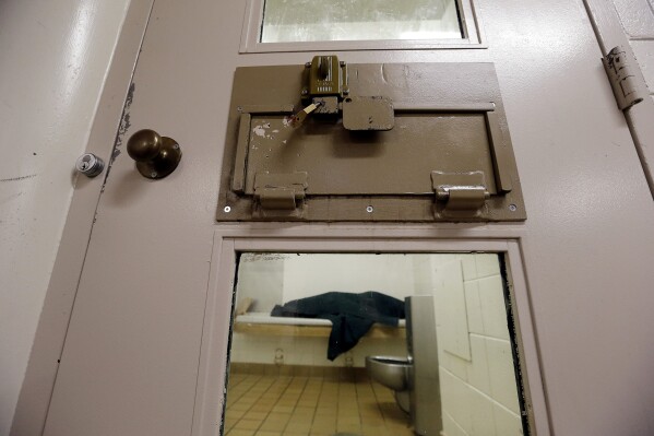 FILE - An inmate huddles under a heavy blanket on a bunk in the psychiatric unit of the Pierce County Jail in Tacoma, Wash, on Oct. 15, 2014. A federal judge has found Washington state in contempt and ordered it to pay more than $100 million in fines for failing to provide timely psychiatric services to mentally ill people who are forced to wait in jails for weeks or months. (AP Photo/Elaine Thompson, File)