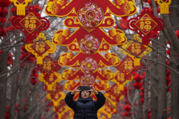 A woman takes a picture of red lanterns and decorations on display along the trees ahead of the Chinese Lunar New Year at Ditan Park in Beijing, Feb. 4, 2024. (AP Photo/Andy Wong)