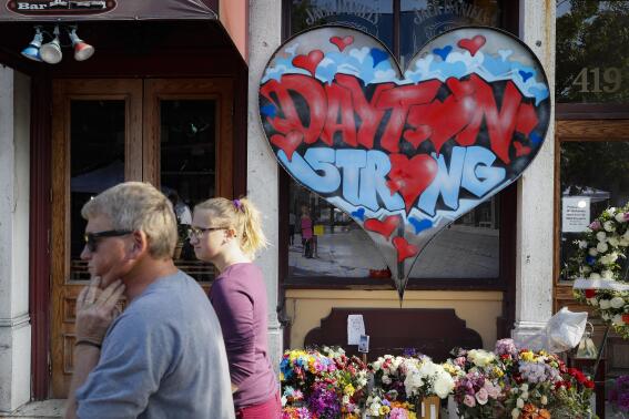 FILE - In this Aug. 7, 2019 file photo, passers-by walk past a makeshift memorial for the slain and injured victims of a mass shooting that occurred in the Oregon District in Dayton, Ohio. Newly released Dayton police records say all of the people killed outside a strip of nightclubs appear to have been shot at random. The FBI finished its investigation late last year without determining whether accused shooter Connor Betts intentionally shot his sister. (AP Photo/John Minchillo, File)