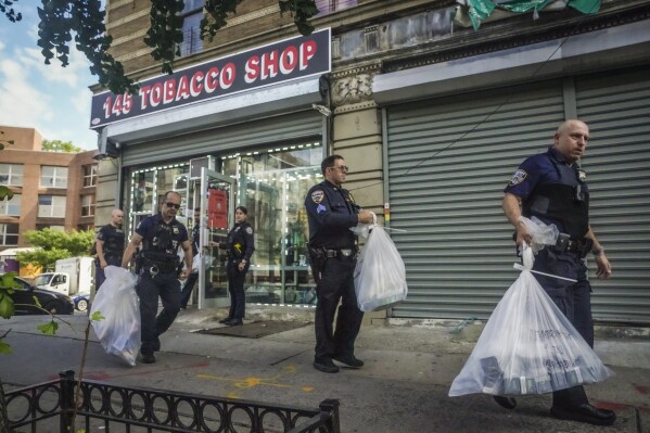 Law enforcement members of New York Sheriff's Joint Compliance Task Force (SJCTF) carry bags of confiscated vaping products, during a spot raid of a tobacco shop, Wednesday Sept. 27, 2023, in New York. Communities across the U.S. are confronting a new vaping problem: how to get rid of millions of disposable e-cigarettes that are considered hazardous waste. The devices contain nicotine, lithium and other materials that cannot be reused or recycled. (AP Photo/Bebeto Matthews)