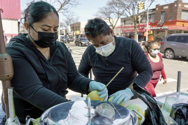 Ruth Palacios and Arturo Xelo, a married couple from Mexico, work at their fruit stand in the Corona neighborhood of the Queens borough of New York on Tuesday, April 13, 2021. They worked seven days a week for months disinfecting COVID-19 patient rooms at the Memorial Sloan Kettering Cancer Center in New York City, but weren't paid overtime Palacios says. The couple filed a federal lawsuit against the contractor that hired them, alleging their pay was cut without their knowledge from $15 an hour to $12.25. They're now selling fruit to make ends meet. (AP Photo/Marshall Ritzel)