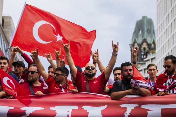 Turkey fans show the 'wolf salute', the origin of which is attributed to a right-wing extremist movement, during a fan walk before the start of the Euro 2024 quarterfinal soccer match between the Netherlands and Turkey in Berlin, Saturday, July 6, 2024. (Christoph Soeder/dpa via AP)