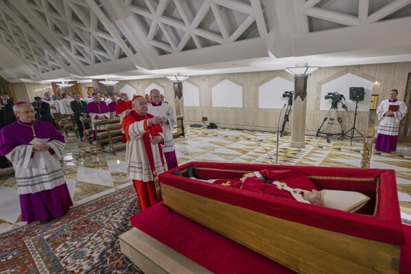 Cardinal Camerlengo Kevin Joseph Farrell, center, flanked by Master of Ceremonies Archbishop Diego Giovanni Ravelli, left, and Master of Ceremonies Lubomir Welnitz, right, performes the ceremonial aspersion of the body of Pope Francis with holy water as part of the final rites inside his private chapel at the Vatican, Monday, April 21, 2025. (Vatican Media via AP, HO)