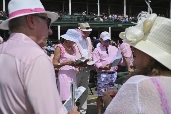 Fans look over racing programs at Churchill Downs before the 151st running of the Kentucky Oaks horse race Friday, May 2, 2025, in Louisville, Ky. (AP Photo/Jon Cherry)