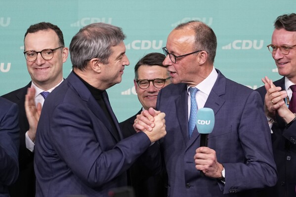 Friedrich Merz, with the microphone, the candidate of the mainstream conservative Christian Democratic Union party, shakes hands with Markus Soeder, leader of CSU and Minister-President of Bavaria, at the party headquarters in Berlin, Germany, Sunday, Feb. 23, 2025, after the German national election. (AP Photo/Martin Meissner)