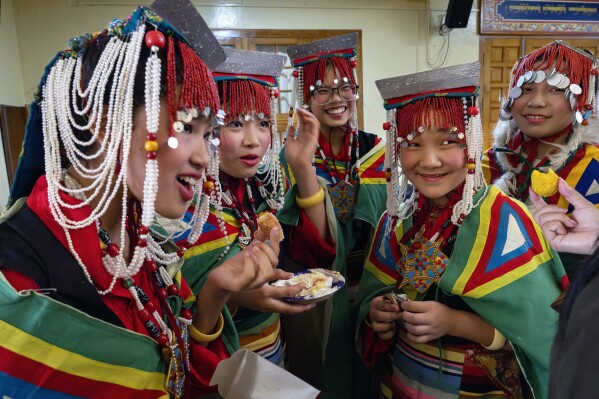 Exiled Tibetan school girls in a traditional costumes eat cakes and sweets as they wait to perform a traditional dance at an event to celebrate the 89th birthday of Tibetan spiritual leader the Dalai Lama at the Tsuglakhang temple in Dharamshala, India, Saturday, July 6, 2024. (AP Photo/Ashwini Bhatia)