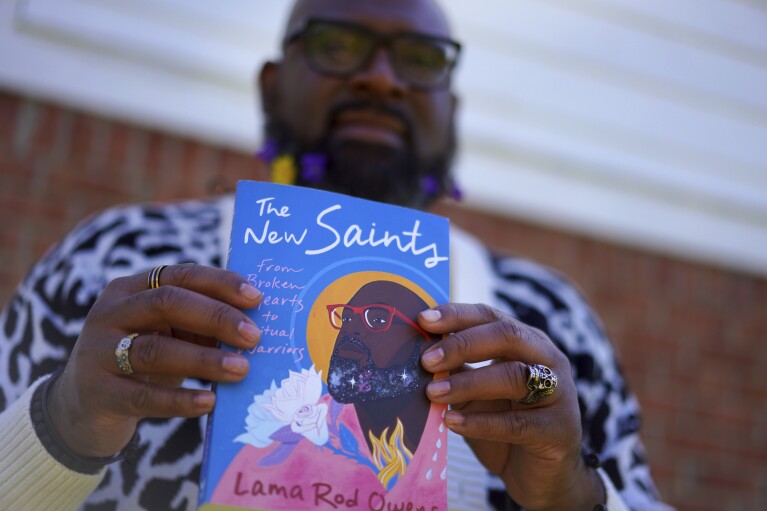 Lama Rod Owens holds his latest book, "The New Saints," which highlights Christian saints and spiritual warriors, Buddhist bodhisattvas and Jewish tzaddikim among those who have sought to free people from suffering on Saturday, March 30, 2024, in Rome, Georgia. (AP Photo/Jessie Wardarski)