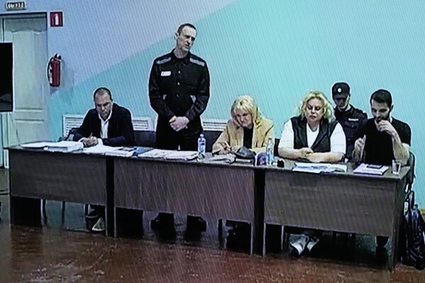 A view of a TV Screen showing Russian opposition leader Alexei Navalny, 2nd left, between his lawyers in a courtroom, via video link provided by the Russian Federal Penitentiary Service, during a preliminary hearing, in Melekhovo, Vladimir region, about 260 kilometers (163 miles) northeast of Moscow, Russia, on Monday, June 19, 2023. A Russian court has opened a new trial of imprisoned Russian opposition leader Alexei Navalny that could keep him behind bars for decades. (AP Photo/Alexander Zemlianichenko)