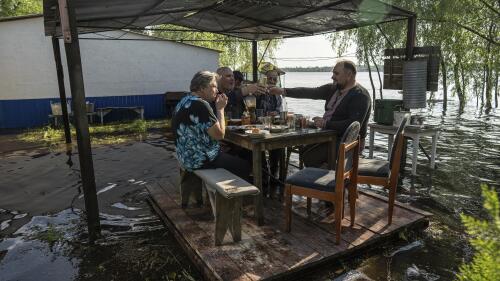 Lyudmila Kulachok, 54, left, with her family have dinner at the flooded courtyard of their house in the island of Kakhovka reservoir on Dnipro river near Lysohirka, Ukraine, Thursday, May 18, 2023. Damage that has gone unrepaired for months at a Russian-occupied dam is causing dangerously high water levels along a reservoir in southern Ukraine. (AP Photo/Evgeniy Maloletka)