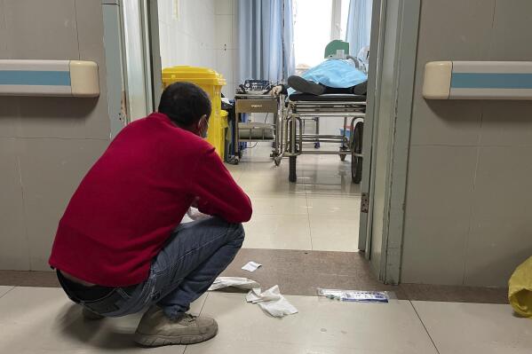 A man squats outside a treatment room as an elderly person receives help with breathing via a manual ventilator pump at the emergency department of the Baoding No. 2 Central Hospital in Zhuozhou city in northern China's Hebei province on Wednesday, Dec. 21, 2022. China only counts deaths from pneumonia or respiratory failure in its official COVID-19 death toll, a Chinese health official said, in a narrow definition that limits the number of deaths reported, as an outbreak of the virus surges following the easing of pandemic-related restrictions. (AP Photo)