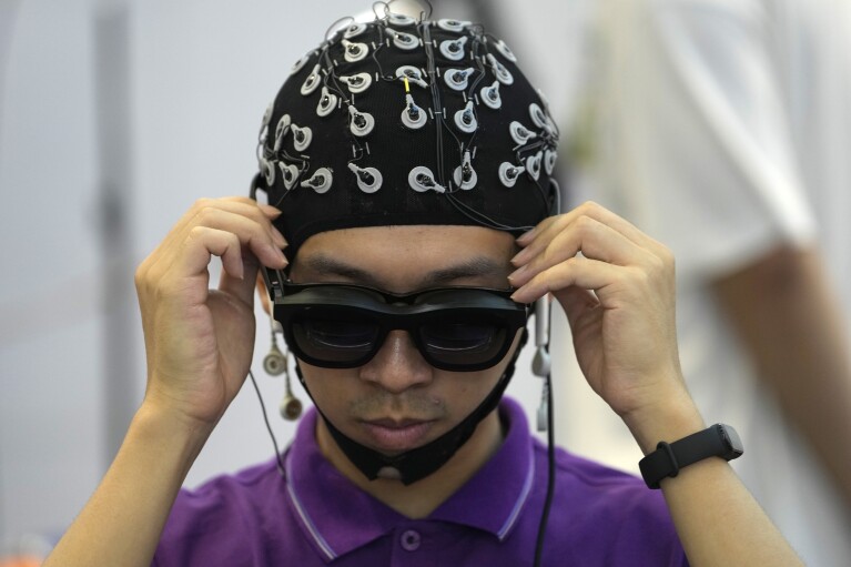A man tests a device that uses brain activities and virtual reality to control other machines at the annual World Robot Conference at the Beijing Etrong International Exhibition and Convention Center, Wednesday, Aug. 16, 2023. (AP Photo/Ng Han Guan)