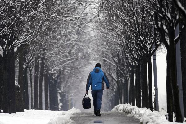 A man walks through a snow covered street in Belgrade, Serbia, Sunday, Feb. 26, 2023. Serbia and the rest of the region were hit by a sudden weather change this weekend that brought rain and snow after a warm period. (AP Photo/Darko Vojinovic)