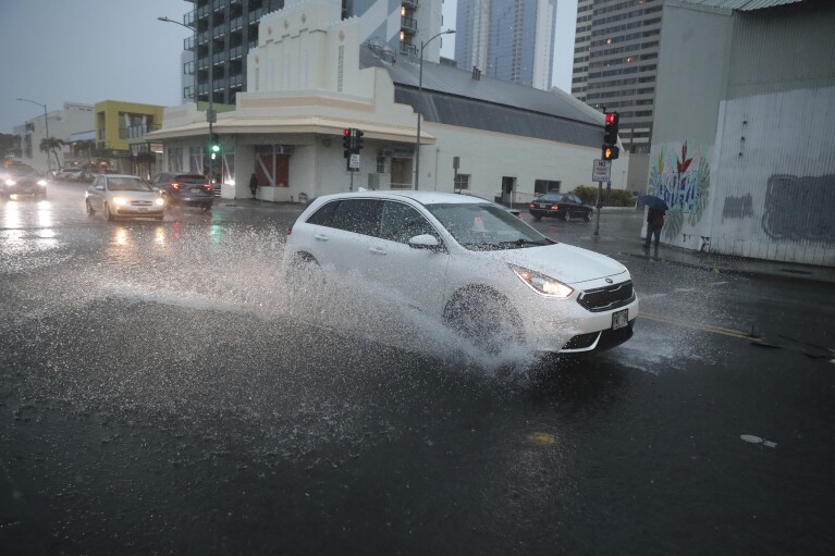 FILE - A car turns onto a flooded Cooke Street, Monday, Dec. 6, 2021, in Honolulu. (AP Photo/Marco Garcia, File)