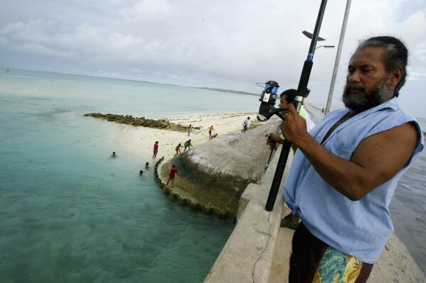 FILE - A man fishes on a bridge on Tarawa atoll, Kiribati, on March 30, 2004. (AP Photo/Richard Vogel, File)