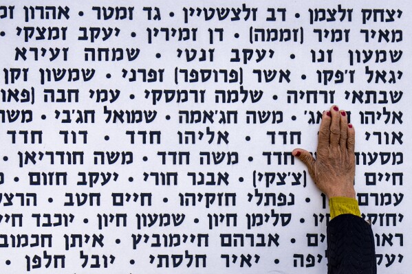 A woman touches the wall with names of fallen soldiers during Israel's annual Memorial Day for the fallen soldiers who died in the nation's conflicts and victims of nationalistic attacks at the Armored Corps memorial site in Latrun, Israel, Monday, May 13, 2024. (AP Photo/Ariel Schalit)