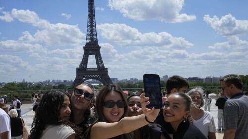 Tourists pose for a selfie with the Eiffel Tower in background, Thursday, July 6, 2023 in Paris. French government officials met with representatives of the tourism industry to discuss repercussions of unrest sparked by the police killing of a 17-year-old boy on tourist activity and on France's international image. The shooting death of Nahel Merzouk, who was of north African descent, prompted nationwide anger over police tactics and entrenched discrimination against people in low-income neighborhoods around France where many trace their roots to former French colonies. (AP Photo/Michel Euler)