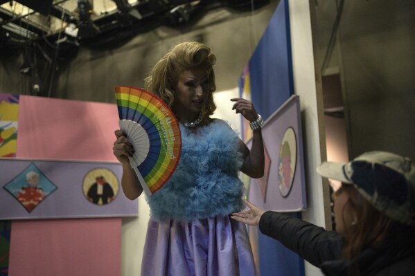 Amanda, the first-ever drag queen to host a news program for Mexican TV, steps off her set while holding a rainbow fan in memory of magistrate Ociel Baena, at the end of her Canal Once newscast "La Verdrag", in Mexico City, Wednesday, Nov. 15, 2023. Donning a blazer, silver pumps shrouded by a white skirt and their signature rainbow fan, it would be the last TV interview the magistrate would ever give. (AP Photo/Aurea Del Rosario)