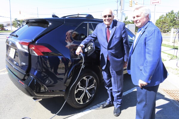 Joseph Fiordaliso, president of the New Jersey Board of Public Utilities, left, and Asbury Park Mayor John Moor, right, speak in front of a new electric vehicle charging station that had not yet been activated in Asbury Park, N.J. on March 21, 2022. Fiordaliso, who was implementing much of New Jersey Gov. Phil Murphy's push for clean energy projects, died on Sept. 6, 2023, at age 78. (AP Photo/Wayne Parry)