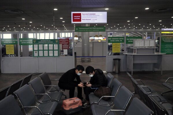 Passengers play their smart phones as they wait at an empty hall inside Sheremetyevo international airport outside Moscow, Russia, Wednesday, March 18, 2020. Authorities in Russia are taking vast measures to prevent the spread of the disease in the country. The measures include closing the border for all foreigners, shutting down schools for three weeks, sweeping testing and urging people to stay home. For most people, the new coronavirus causes only mild or moderate symptoms. For some it can cause more severe illness. (AP Photo/Pavel Golovkin)