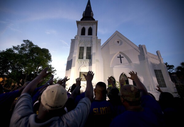 FILE - Members of the Omega Psi Phi Fraternity lead a crowd of people in prayer outside the Emanuel African Methodist Episcopal Church after a memorial for the nine people who were shot and killed during Bible study in Charleston, S.C., Friday, June 19, 2015. When violence comes to a public place, as it does all too often in our era, a delicate question lingers afterward: What should be done with the buildings where blood was shed? (AP Photo/Stephen B. Morton, File)