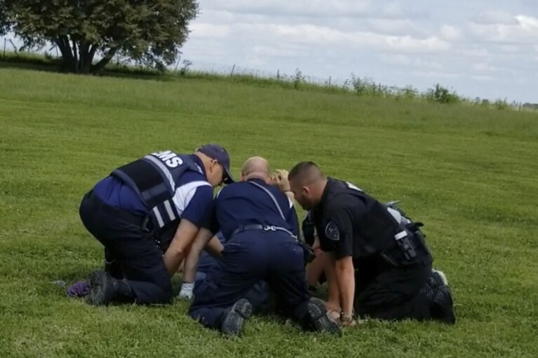 In this image from video provided by a family friend, Taylor Ware is restrained by law enforcement and emergency medical personnel at a highway rest stop in Dale, Ind., on Aug. 25, 2019. Taylor's mother called 911 when he wouldn’t get back in their SUV during a manic episode caused by bipolar disorder. A cascade of force ended with Ware in a coma. He died three days later. (Pauline Engel via AP)