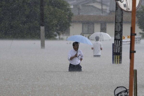FILE - People wade through a street due to a heavy rain in Kurume, Fukuoka prefecture, southern Japan on July 10, 2023. Scientists say increasingly frequent and intense storms could unleash more rainfall in the future as the atmosphere warms and holds more moisture. (Kyodo News via AP, File)