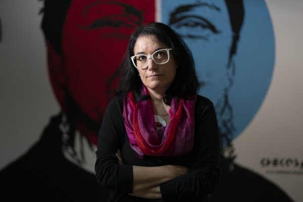 Marilu Mastrogiovanni poses in front of a murales dedicated to Gloria Anzaldua, an American scholar of Chicana feminism, cultural theory, and queer theory, during an interview at the Bari's university, Monday, May 20, 2024. Investigative journalist, Professor of Investigative Journalism, has reported extensively on the infiltration of the Sacra Corona Unita in the local community and city hall for her blog "Tacco d'Italia." Her reports so angered the local government that they plastered the town with giant posters attacking her work and one depicted her up to her neck in a hole in the ground. After various threats, she was put under police escort and eventually decided to move her family to Bari where she now teaches investigative journalism in the Master in Journalism course at the University of Bari. (AP Photo/Alessandra Tarantino)
