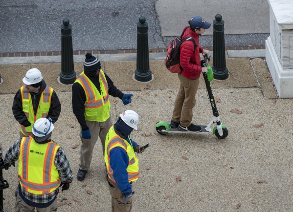
              In this Dec. 5, 2018, photo a rider maneuvers a Lime brand electric scooter on a sidewalk past workers on Capitol Hill in Washington. Electric scooters are overtaking station-based bicycles as the most popular form of shared transportation outside transit and cars. (AP Photo/J. Scott Applewhite)
            