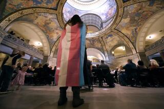 FILE - Glenda Starke wears a transgender flag as a counterprotest during a rally in favor of a ban on gender-affirming health care legislation, March 20, 2023, at the Missouri Statehouse in Jefferson City, Mo. Minors in Missouri soon will be required to undergo 18 months of therapy before receiving gender-affirming health care under an emergency rule released Thursday, April 13, 2023, by the state's Republican attorney general. (AP Photo/Charlie Riedel, File)