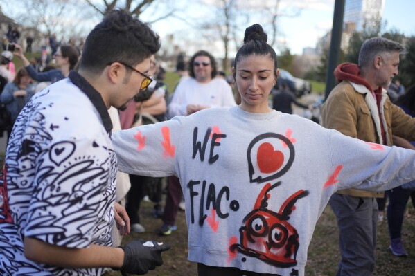 Calicho Arevalo, left, paints a message about Flaco the Eurasian eagle-owl on Alex Osorio's sweatshirt during a memorial for Flaco in Central Park in New York, Sunday, March 3, 2024. Mournful fans of Flaco have gathered in New York City to say goodbye to the beloved celebrity creature who became an inspiration and joy to many as he flew around Manhattan after he was let out of his zoo enclosure. (AP Photo/Seth Wenig)