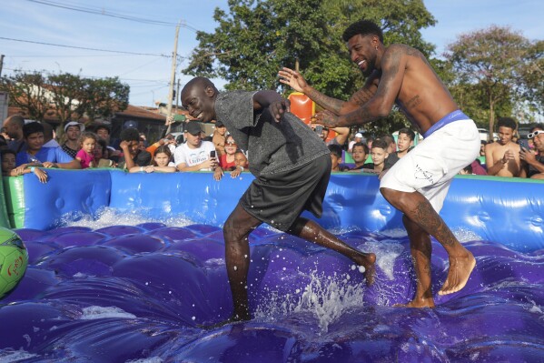 La celebridad de TikTok Khaby Lame (izquierda, centro) y el futbolista brasileño Emerson Royal juegan al fútbol en una piscina hinchable durante un acto para donar juguetes para niños, en Americana, Brasil, el 13 de junio de 2025. (AP Foto/Andre Penner)