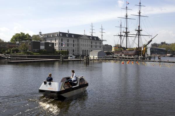 An electric boat steers close to a full-size replica of the 18th century three-mast trading ship Amsterdam at the National Maritime Museum, in Amsterdam, Thursday, May 20, 2021. Already steeped in maritime history, the city's more than 100 kilometers (60 miles) of waterways are to start hosting prototypes of futuristic boats — small, fully-autonomous electric vessels — to carry out tasks including transporting passengers and picking up garbage. (AP Photo/Peter Dejong)