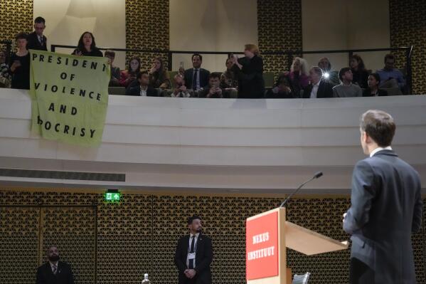 French President Emmanuel Macron looks at demonstrators unfolding a banner reading "President of Violence and Hypocrisy" as he explains his vision on the future of Europe during a lecture in a theatre in The Hague, Netherlands, Tuesday, April 11, 2023. (AP Photo/Peter Dejong)