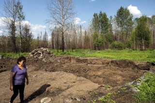 Carrol Johnston passes an indentation where her home stood before a May wildfire destroyed it in the East Prairie Metis Settlement, Alberta, on Tuesday, July 4, 2023. Johnston, who has been living in a nearby town, is awaiting a modular home so she can return to the land. (AP Photo/Noah Berger)