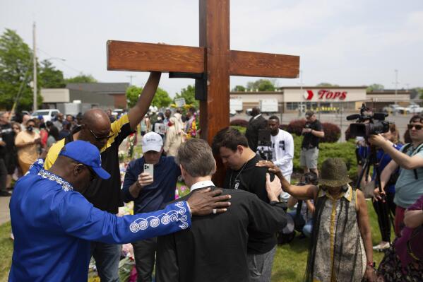 A group prays at the site of a memorial for the victims of the Buffalo supermarket shooting outside the Tops Friendly Market on Saturday, May 21, 2022, in Buffalo, N.Y.   Tops was encouraging people to join its stores in a moment of silence to honor the shooting victims Saturday at 2:30 p.m., the approximate time of the attack a week earlier. Buffalo Mayor Byron Brown also called for 123 seconds of silence from 2:28 p.m. to 2:31 p.m., followed by the ringing of church bells 13 times throughout the city to honor the 10 people killed and three wounded. (AP Photo/Joshua Bessex)