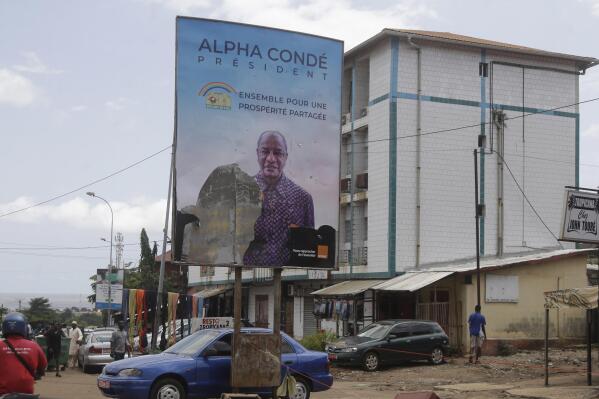 People walk past a defaced billboard with former Guinea's President Alpha Conde, on a street in Conakry, Guinea, Thursday, Sept. 9, 2021. Guinea's new military leaders sought to tighten their grip on power after overthrowing President Alpha Conde, warning local officials that refusing to appear at a meeting convened Monday would be considered an act of rebellion against the junta. (AP Photo/Sunday Alamba)